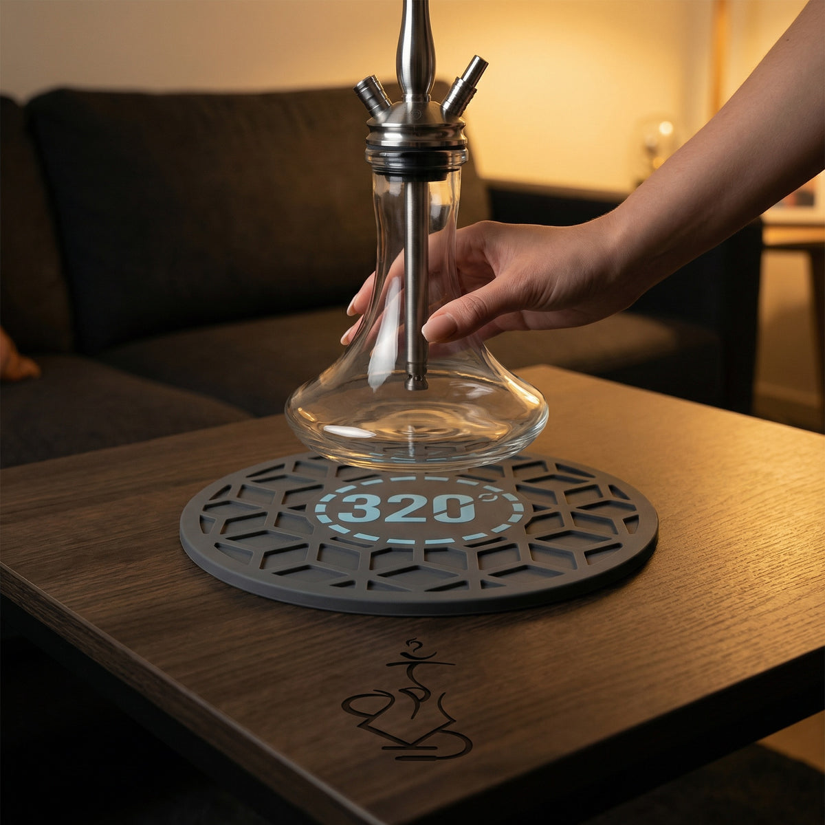 320° Hookah Base Mat Black & Blue placed on a dark timber lounge table with a glass hookah base being set down onto the grip surface, showing the mat in a real session setup., image 8 of 15