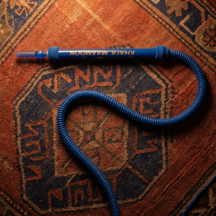 Khalil Mamoon Blue Shisha Hose resting on a warm Persian kilim in a quiet majlis setting