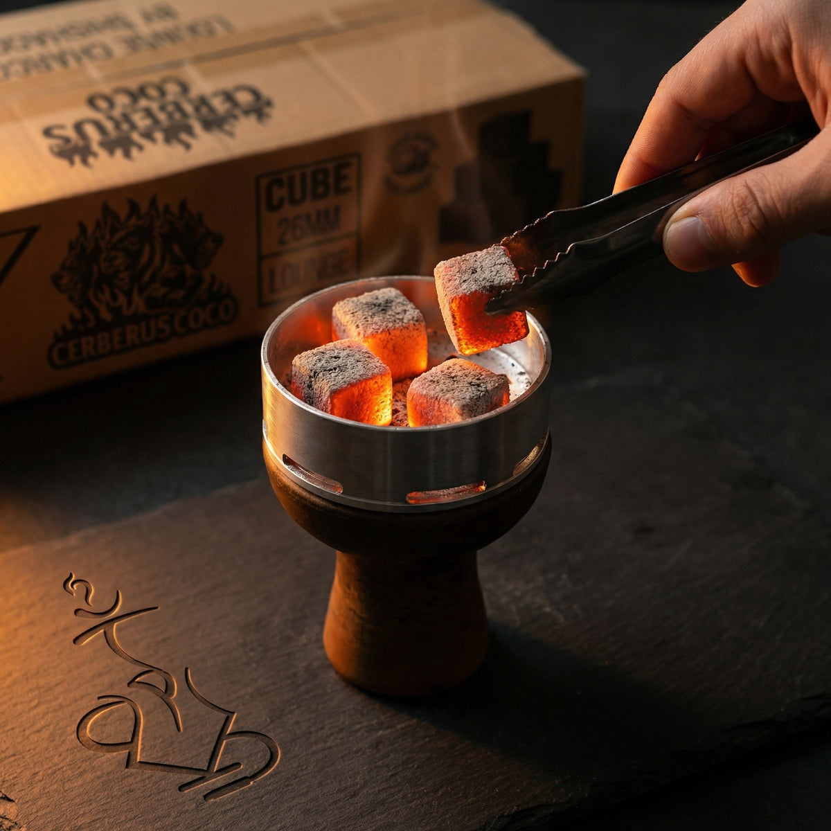  Glowing Cerberus Coco 26mm coconut shisha charcoal cubes inside a heat management device on a hookah bowl, hand placing a coal with tongs during a session., image 7 of 11