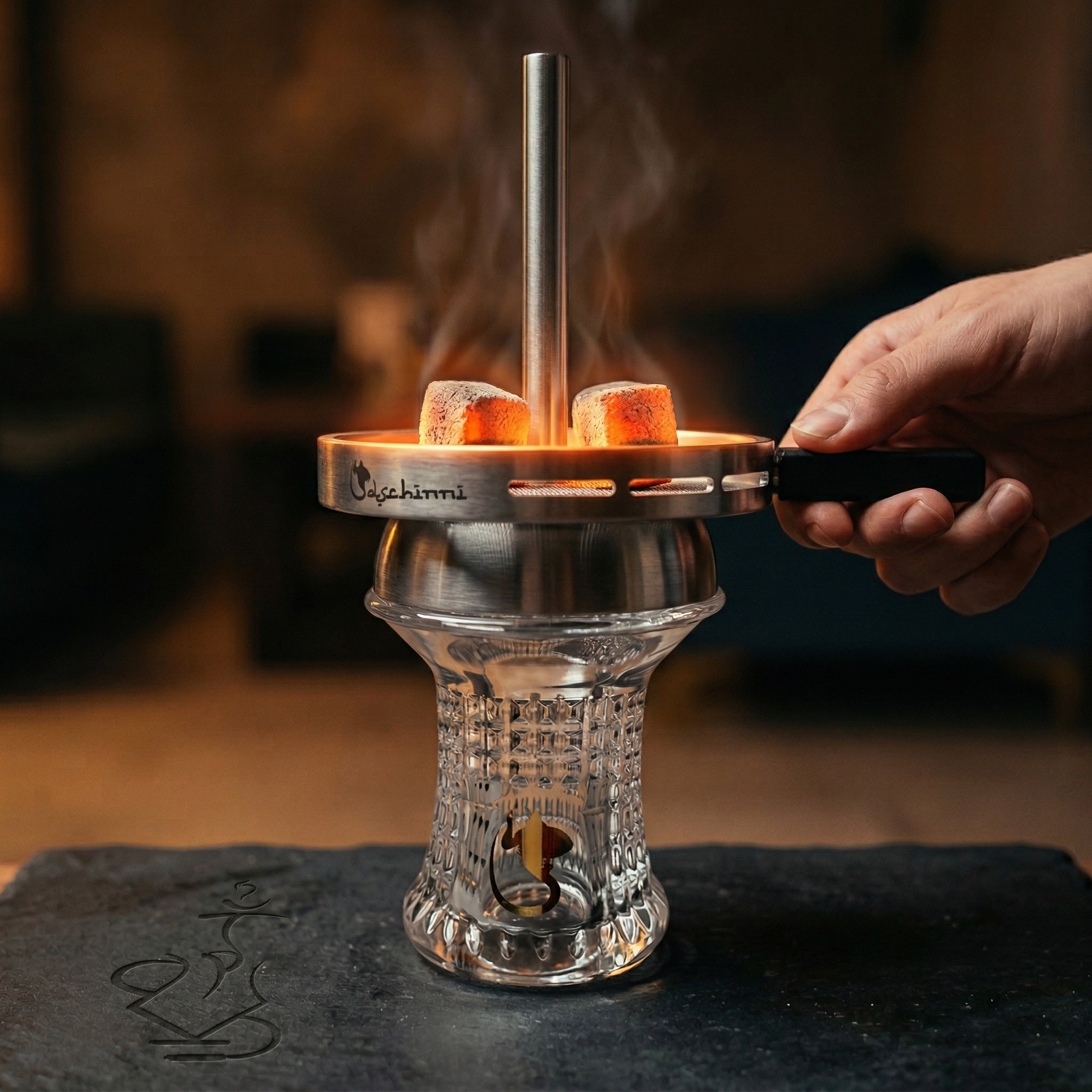 Dschinni Nero Glass Head Bundle assembled in a hookah session with glowing coals inside the Vulcan Air 2.0 chimney, hand adjusting the handle, warm lounge atmosphere.