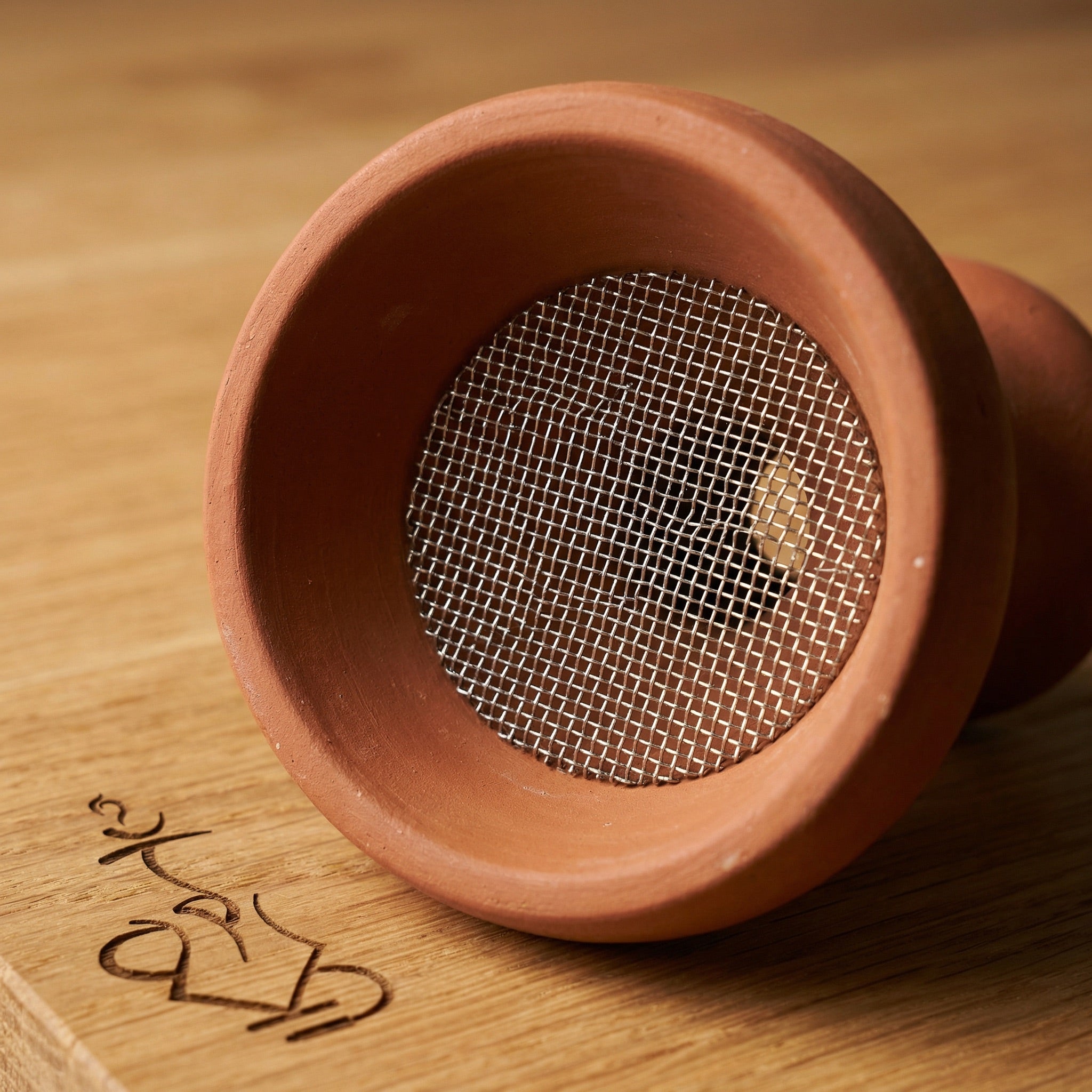 Essentials stainless mesh insert seated flat inside a traditional multi-hole Egyptian clay shisha bowl, showing the fit and coverage over the draw holes for cleaner base water.