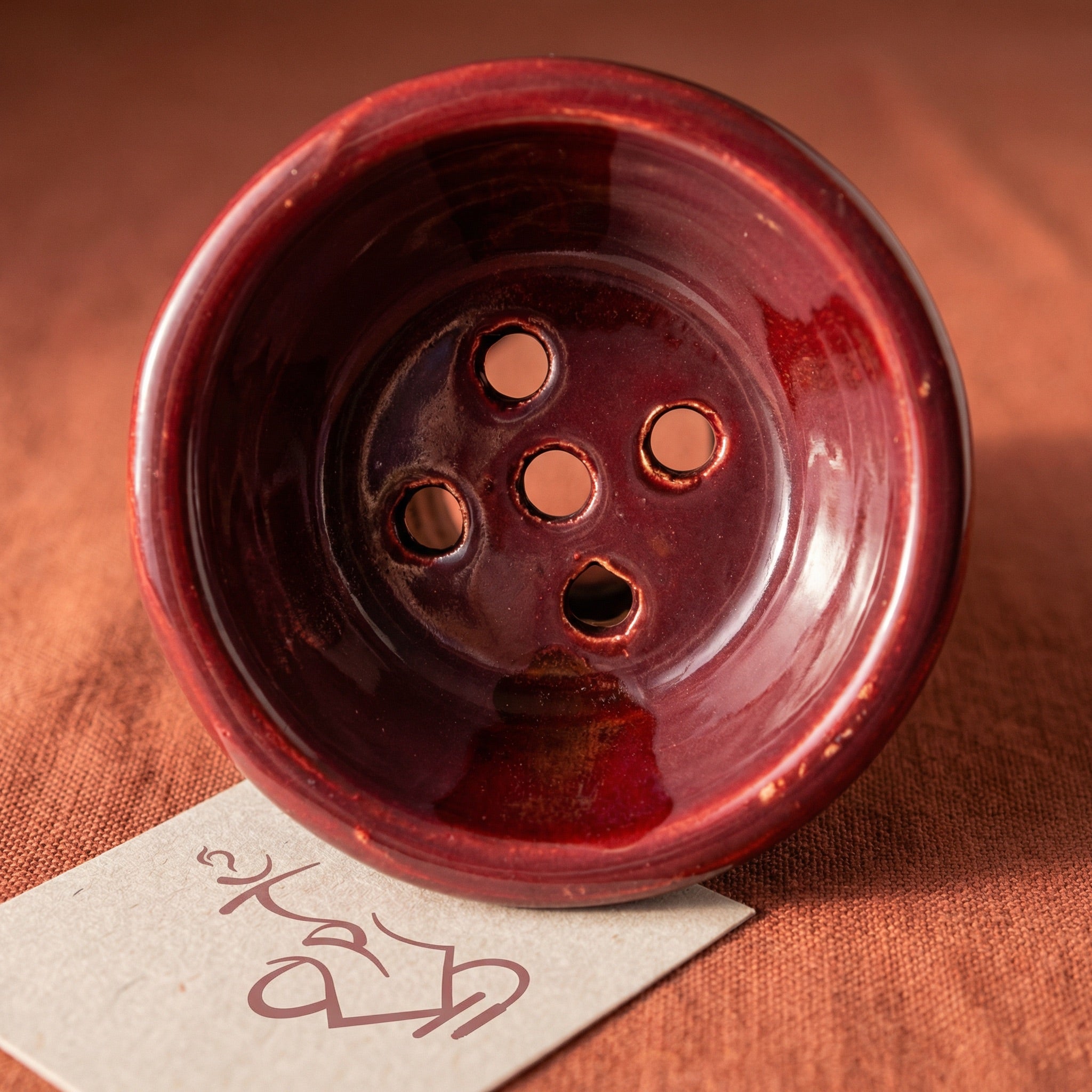 Top-down macro of the King Buzz Traditional Egyptian Bowl interior showing the 5-hole floor pattern and hand-dipped burgundy ceramic glaze texture.