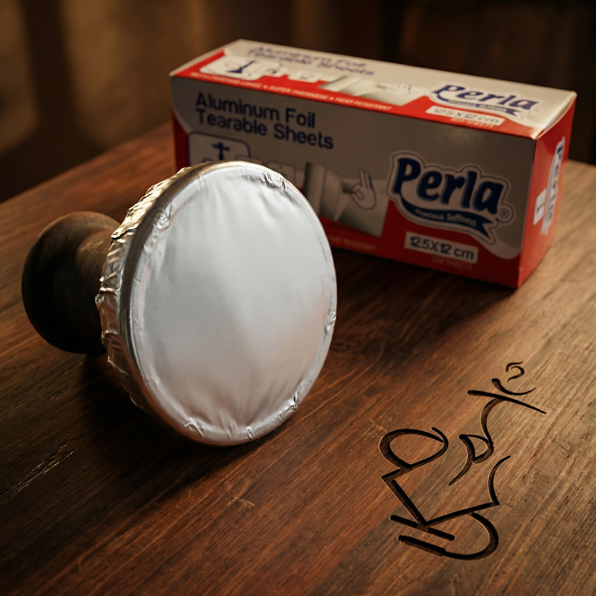 Perla Heavy-Duty Shisha Foil sheet stretched tightly over the rim of a standard clay phunnel hookah bowl, ready for hole-poking, with the dispenser box visible behind.