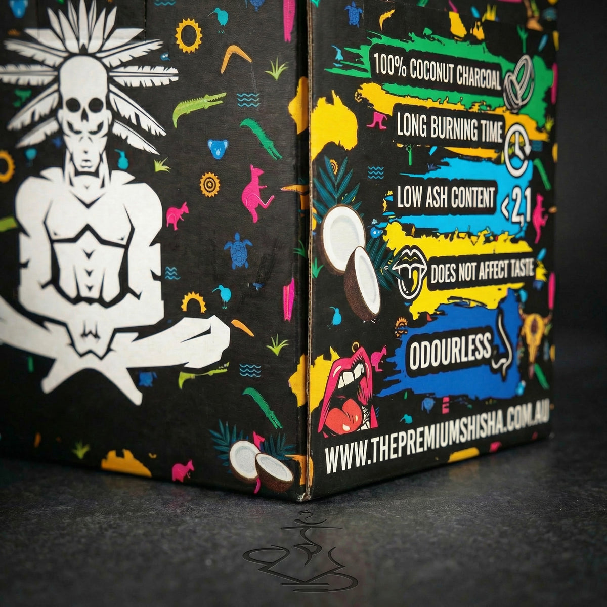 Close-up detail of Shaman 26mm coconut charcoal 1kg box corner showing the seated skull mascot meeting the colourful features panel with product claims., image 4 of 15