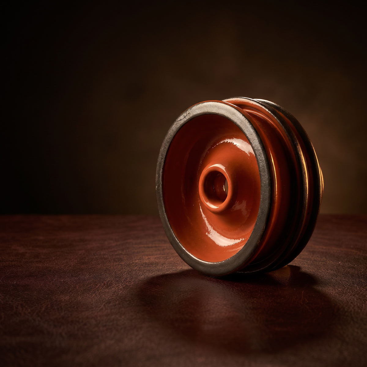 Diablo Rust phunnel shisha bowl on oxblood leather, warm rim light highlighting terracotta glaze and dark clay bands, The Premium Way, image 2 of 6
